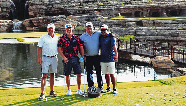4 advisors stand together smiling, on a golf course