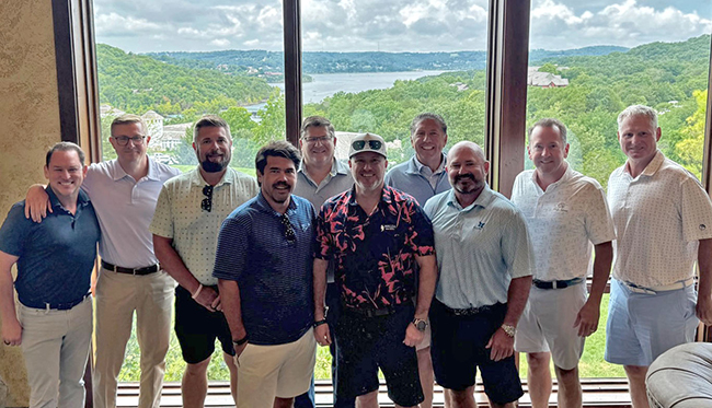 A group of advisors stand together smiling at a roundtable meeting