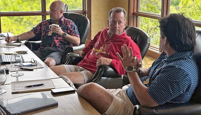3 advisors sit at a conference table, having a discussion