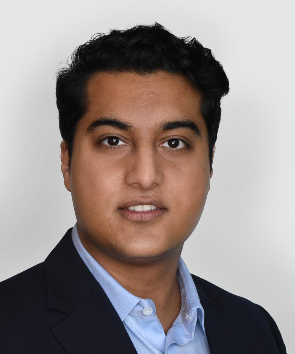 Headshot of Khurram Naveed, wearing a light blue shirt and dark blue blazer, with a plain gray background