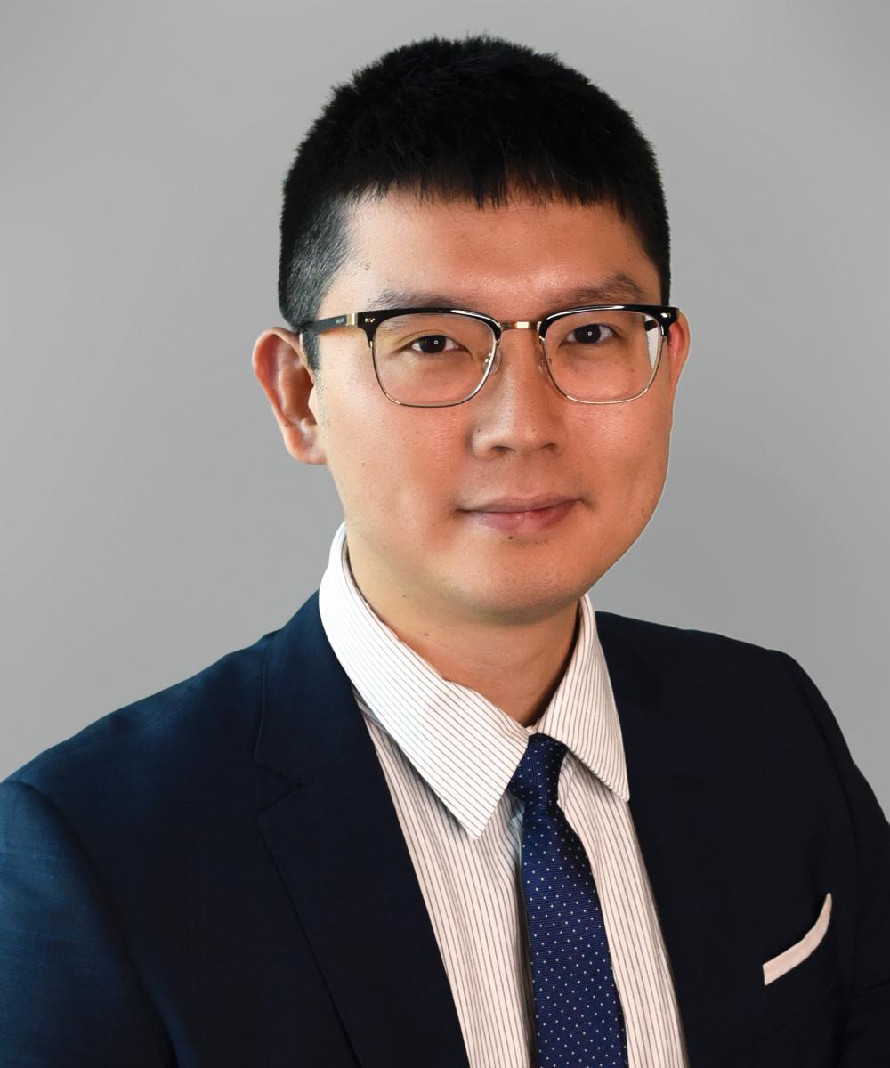 Headshot of Liyin Bao, wearing a white shirt, blue tie, and blue blazer, with a plain gray background